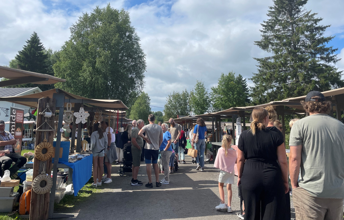Two rows of market stalls on a gravel road with people strolling around 