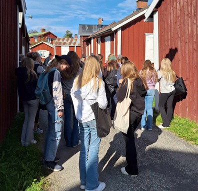 En grupp högstadieelever står bland kyrkstugorna en solig dag.